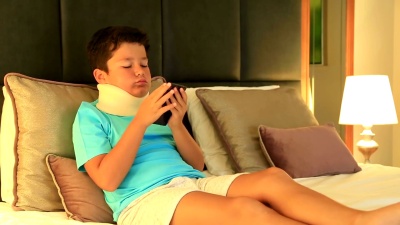 使用智能手机戴着颈托的不开心、无聊的小男孩