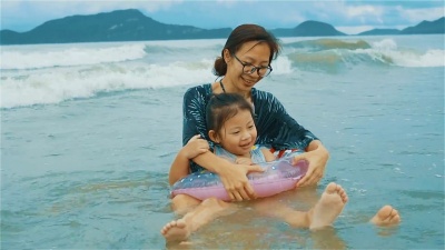 亚洲年轻的母亲和女儿拥抱在海滩上的海浪中玩耍