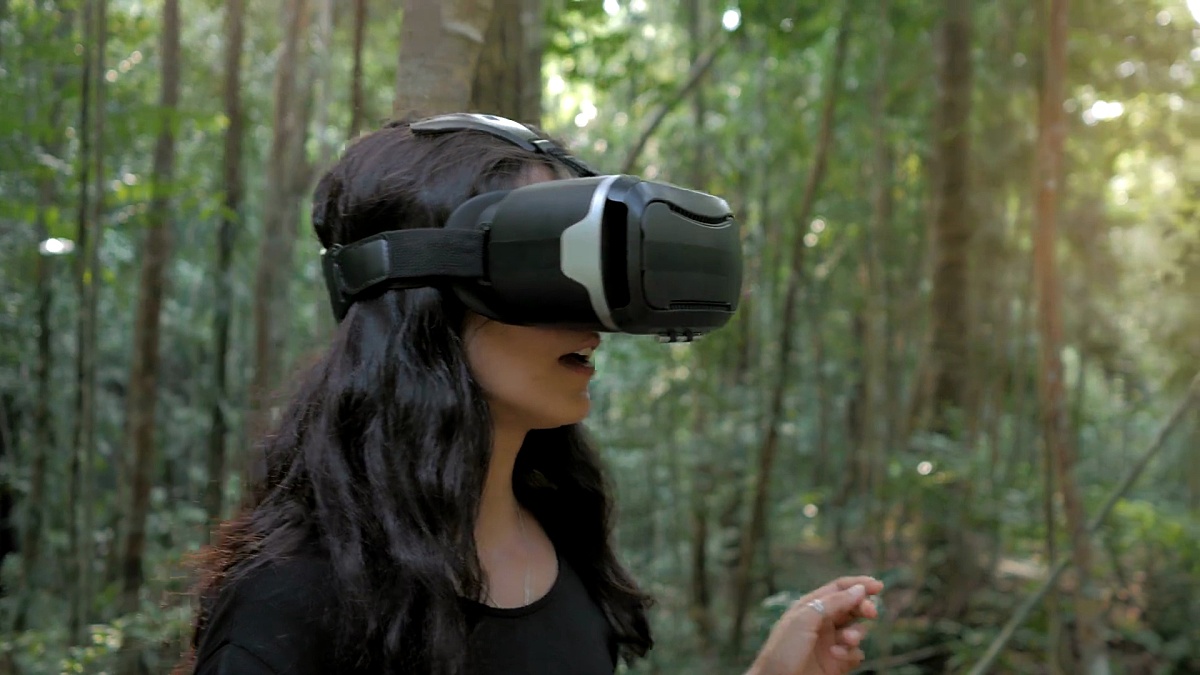 美丽的年轻黑发女子在丛林中使用虚拟现实眼镜