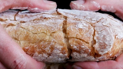 Slow motion of hands breaking a freshly baked loaf of bread