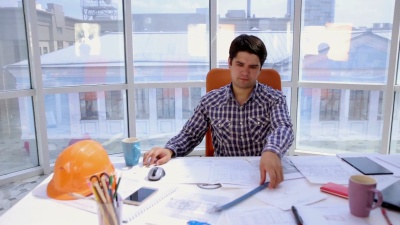 年轻的建筑师，商人，在现代明亮干净的办公室与蓝图和平面图一起工作