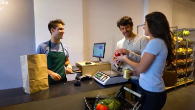 一对幸福的夫妇在食品店结账，男收银员在系统上登记产品，并把它们放在一个纸袋里