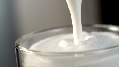 牛奶流掉进装满泡沫牛奶的玻璃杯里