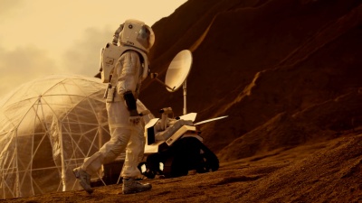 宇航员上山探索红色星球/火星。在背景中，他的基地和AI驱动的火星车。未来殖民概念。