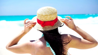 白色海滩上的夏日假期戴着帽子的美女的背影。