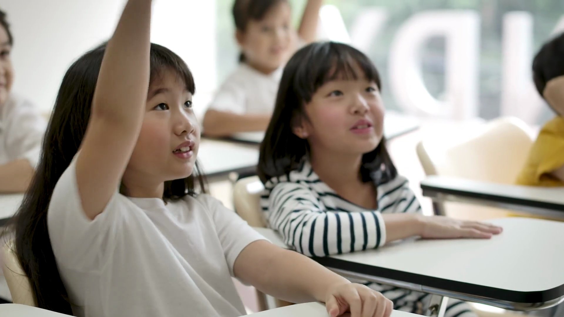 一群快乐的亚洲小学生在课堂上举起手臂回答老师的问题。幼儿园学前概念。