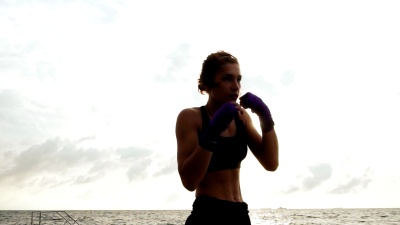 健美的年轻女子在海边对着太阳打太极拳。美女拳击手上午沙滩训练，慢动作挥拳