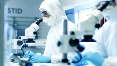 两名穿着无菌洁净服的工程师/科学家/技术人员使用显微镜进行组件调整和研究。他们在一家电子元件制造厂工作。