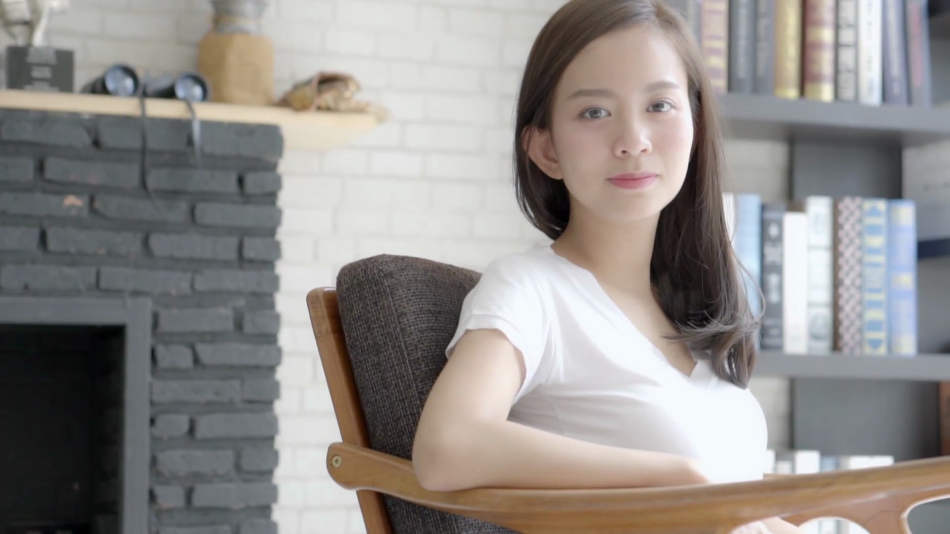 美丽的肖像年轻的亚洲女子微笑着坐在椅子上，快乐地坐在起居室里，移动着摇摄相机，女孩带着自信放松，快乐地看着相机，生活方式理念，慢动作。