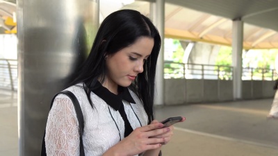 穿白衬衫的亚洲年轻女商人站着通过智能手机发短信