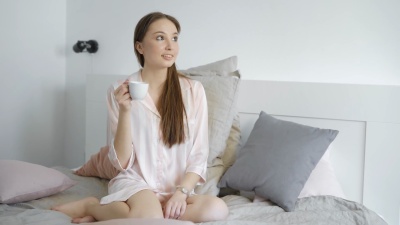 一个浪漫的女孩早上坐在床上，用白色的小杯子喝咖啡，做梦