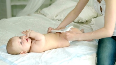 母亲给婴儿穿衣服。一位年轻的母亲和一个六个月大的孩子。妈妈穿尿布，牛仔裤和衬衫，袜子。