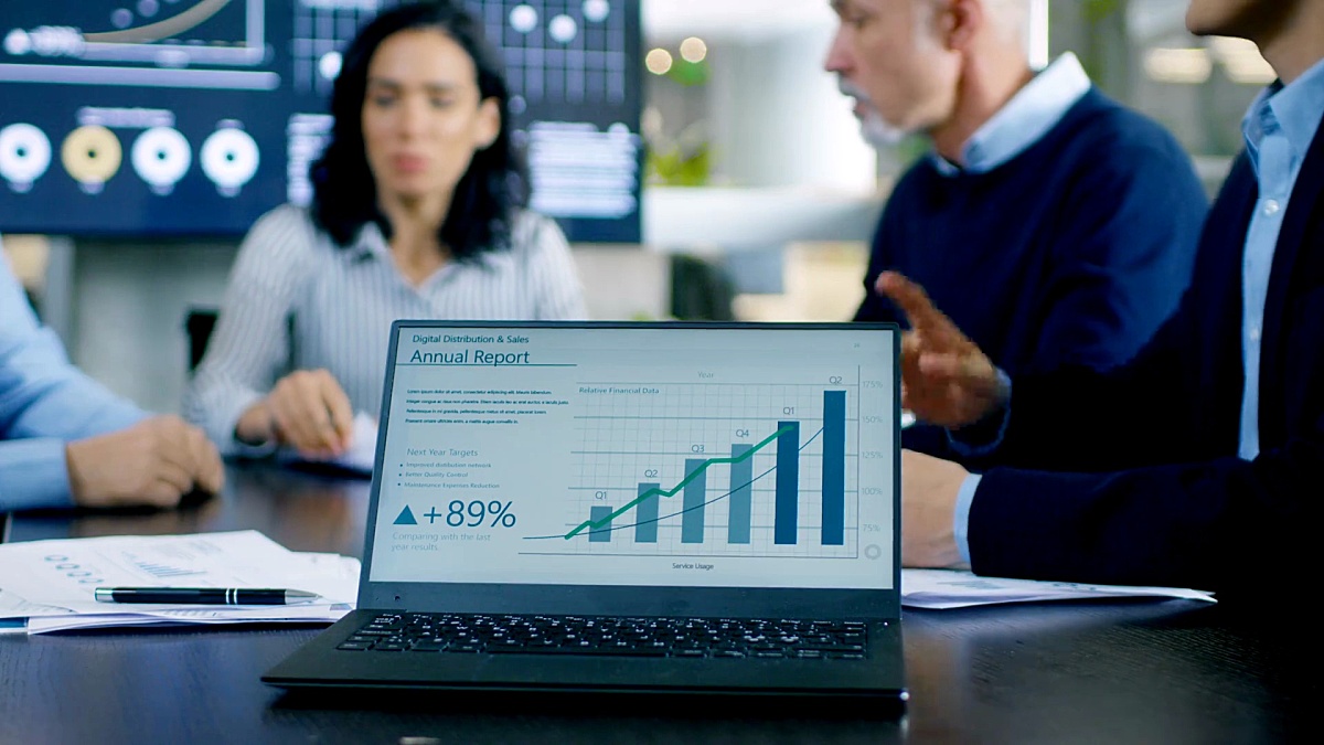 在会议室中，会议桌上的笔记本电脑显示公司的年度增长报告和交互式图表。在背景中，商务人士有重要的讨论。