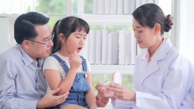 医学，牙科和保健概念-牙医在牙科临床向儿童患者和她的父亲展示牙齿模型。中国香港的医疗系统