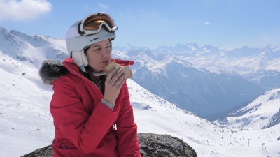 女滑雪者坐在山上滑雪场的石头上吃三明治