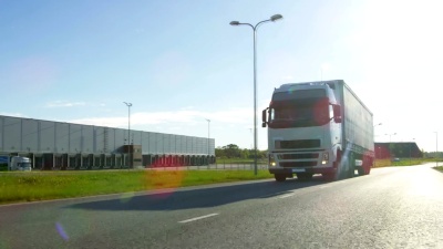 白色半挂车与货物拖车在空旷的道路上。工业仓库旁的高速公路和阳光普照。