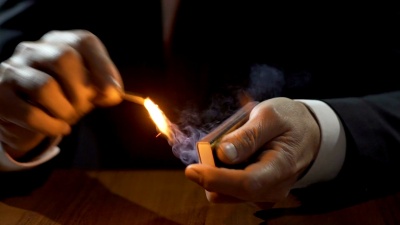穿着昂贵西装的有钱人用火柴点燃古巴雪茄，吸烟的男性