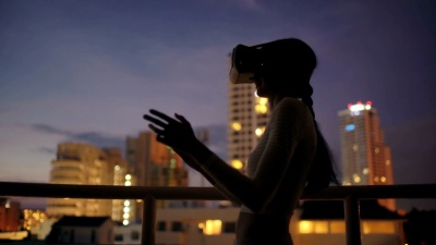 在屋顶露台上使用虚拟现实头盔并在夜间进行VR体验的年轻女子