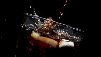 将可乐苏打水倒入一杯冰中，在黑色背景下以慢动作飞溅