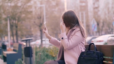 美丽的年轻女子在户外用智能手机自拍时调整长发