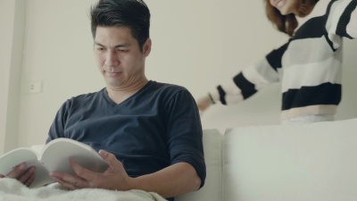 亚洲夫妇一起坐在沙发上看书。