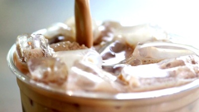 CU Hand-held Camera of Pouring fresh milk tea into a plastic glass of ice.