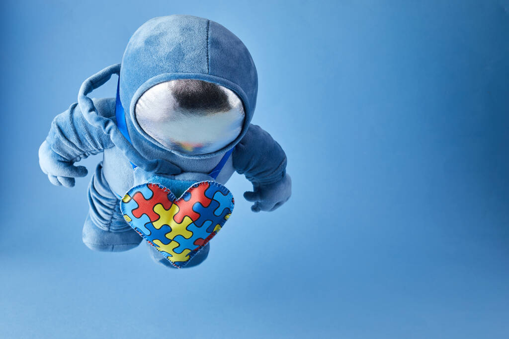 世界自闭症意识日背景。蓝色绒毛航天员玩具，有拼图心，自闭症符号，蓝色背景