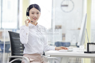 人物系列写实坐在办公室的电脑前带着耳机面带笑容的女性客服
