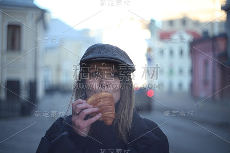 年轻漂亮的女孩在街上吃牛角面包