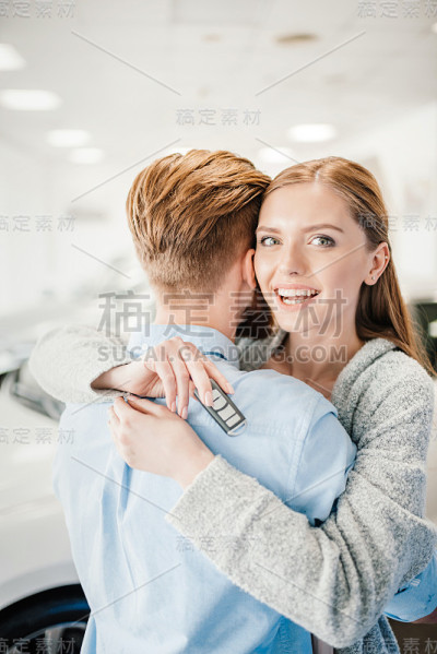 幸福的夫妇拿着车钥匙拥抱在经销商沙龙