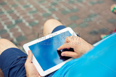 一名男子坐在长凳上用着平板电脑