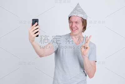 快乐的年轻人戴着锡箔帽自拍并展示和平标志