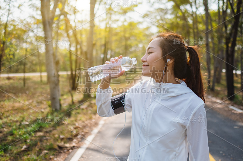 一位亚洲女性跑步者在城市公园慢跑后喝瓶子里的水