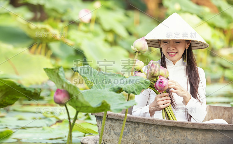 一个越南女人手里拿着一朵莲花。美丽的越南人在越南湖的木船上抱着粉红莲花。