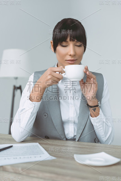 迷人的女商人喝着咖啡闭着眼睛孤立在灰色