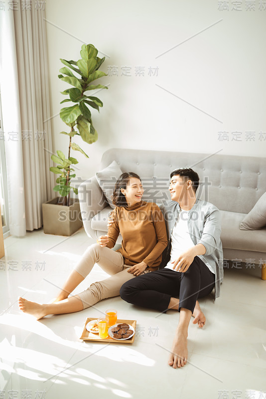 在家放松。快乐的年轻男女喝着热饮和甜糕点。他们坐在沙发附近的桌子旁，面带微笑