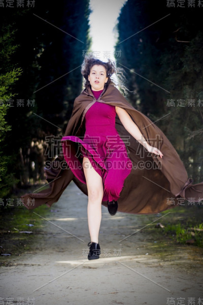 穿着斗篷的漂亮女人出现在树林里的小路上