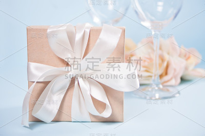 礼品盒与空的两个酒杯和鲜花的背景。浪漫晚餐的概念。