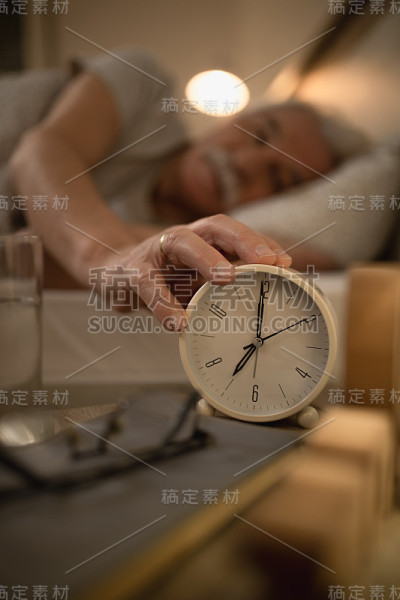 一个成熟男人在床头柜上关掉闹钟的特写。