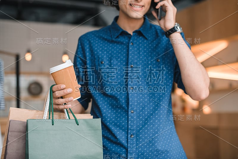 一名年轻人拿着购物袋和纸杯在用智能手机聊天