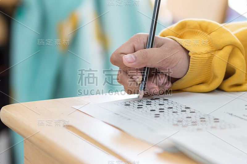 高中生或大学生手拿试卷，在答题纸上写试卷，标准化考试光学形式放在桌上，在教室里做期末考试。教育素养的