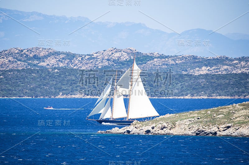 一艘美丽的帆船在地中海上航行，沐浴着撒丁岛海岸。背景是意大利撒丁岛的马达莱娜群岛国家公园。