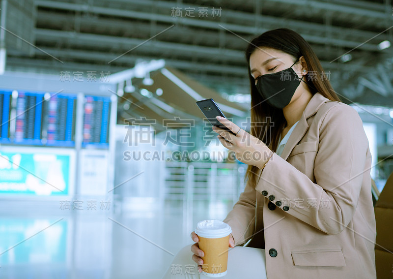 一名年轻的亚洲女子坐在机场等待航班，手里拿着咖啡和手机。