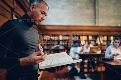 聪明的知识分子男性律师阅读书籍，使研究员的工作，而站在公共图书馆，沉思集中记者分析有趣的信息，从文献