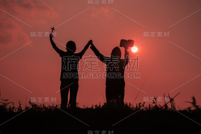 两个少女用圣经向上帝祈祷的剪影。