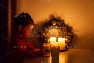 卷毛亚洲男孩拿着蜡烛坐在黑暗中