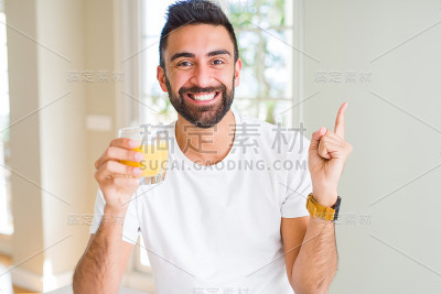 英俊的西班牙人喝着健康的橙汁，非常高兴的指着手和手指的一边