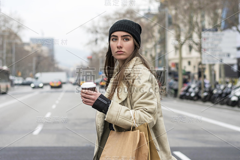 一名年轻的欧洲女子走在城市街道上，手里拿着外卖的咖啡