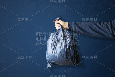 手握深蓝色垃圾袋，清洁地球地球的概念，隔着彩色的墙，简单的概念