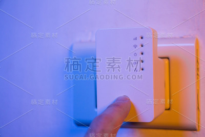 男子将手指按在WiFi中继器的WPS按钮上，该按钮位于墙上的电源插座上